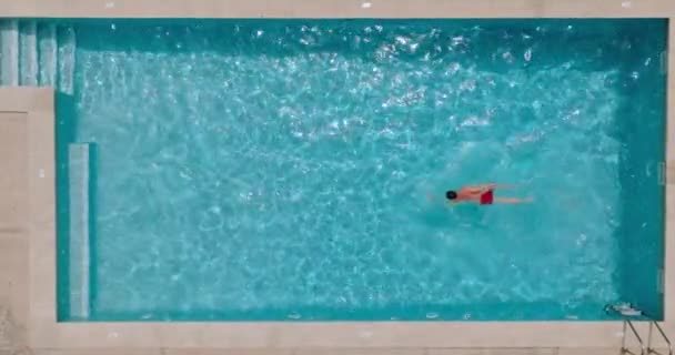Vista de arriba hacia abajo de un hombre en pantalones cortos rojos nada en la piscina. Estilo de vida. Movimiento lento - Metraje, vídeo