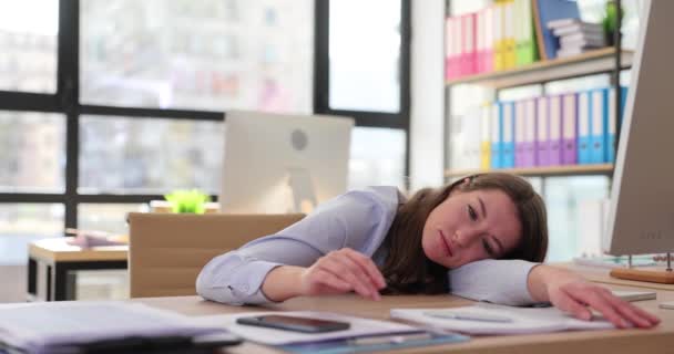Tired woman puts head on table looking at time on mobile phone waiting for end of working day. Fatigue of work and overwork at workplace in corporation slow motion - Footage, Video