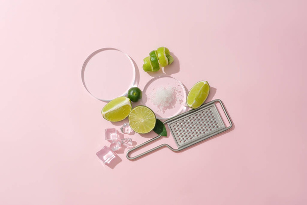 Sea salt is displayed on a glass platform, surrounded by ice and fresh lemons, a grater on a pastel pink background. Lemon is an effective skin beautifying food, treating acne and dark scars - Photo, Image