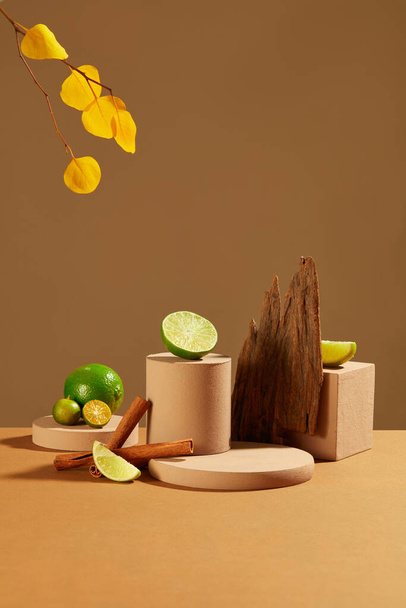 Op een bruine achtergrond zijn roze houten platformen te zien met citroenen, kumquats, kaneel en herfstbladeren. Lege podium voor product display. - Foto, afbeelding