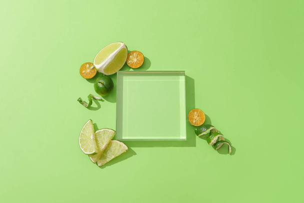 A transparent glass podium is placed on a green background, surrounded by fresh lemons and kumquats. Empty podium for displaying natural products. - Photo, Image