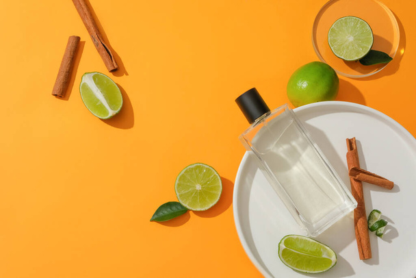 Transparent perfume bottle on a white plate with cinnamon, lemon, and kumquat against a vibrant backdrop. Delicate plant-based fragrance. Copy space for captivating ads. - Photo, Image
