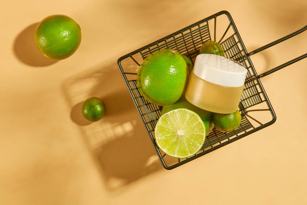 An unlabeled cosmetic jar is placed in an iron basket with fresh lemons and kumquats. The acid in lemon can reduce facial scars. Mockup for vegan cosmetics advertisement. - Photo, Image