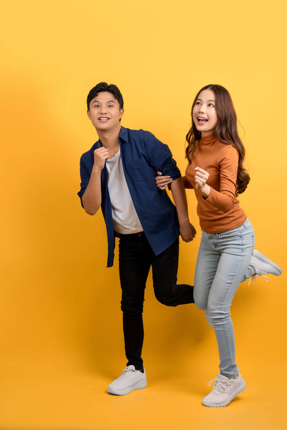 Glücklich lächelndes asiatisches Paar mit Überraschung isoliert auf gelbem Studiohintergrund. - Foto, Bild