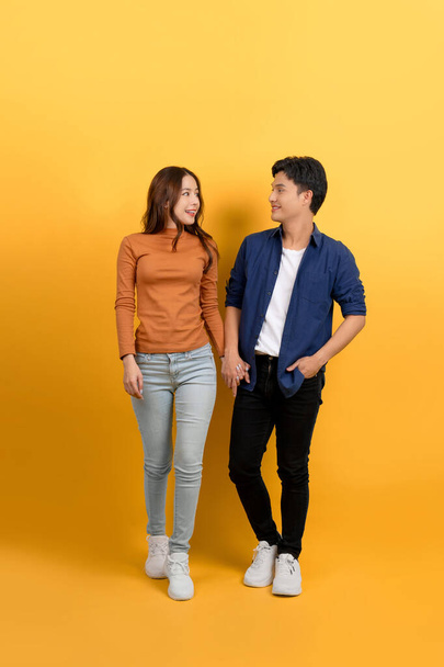 Full view of young Asian couple walking holding hands on blue background. - Photo, Image