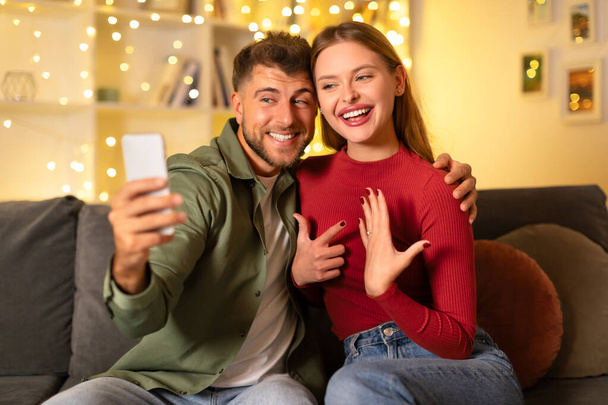 Strahlendes junges Paar macht Selfie, um ihr Verlobungsglück festzuhalten, mit flimmernden Lichtern, die ihrem besonderen Moment Magie verleihen - Foto, Bild