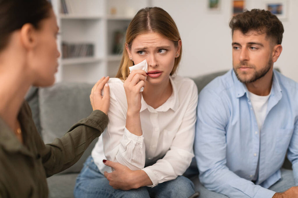 Terapeutka delikatnie pociesza płaczącą kobietę podczas sesji terapeutycznej dla par, podkreślając współczujące wsparcie w małżeńskich zmaganiach w gabinecie psychologów - Zdjęcie, obraz