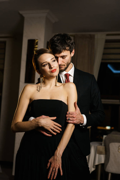 A stylish man and woman in evening wear, a suit and a dress, posing against the backdrop of a luxurious hotel. Casino concept - Photo, Image