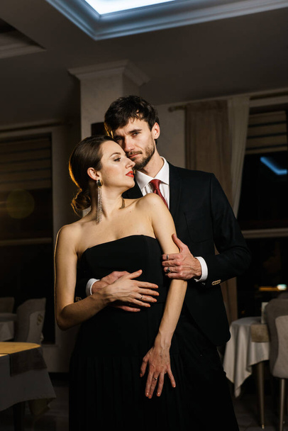 Um homem e uma mulher elegantes em trajes noturnos, um terno e um vestido, posando contra o pano de fundo de um luxuoso hotel. Conceito de casino - Foto, Imagem