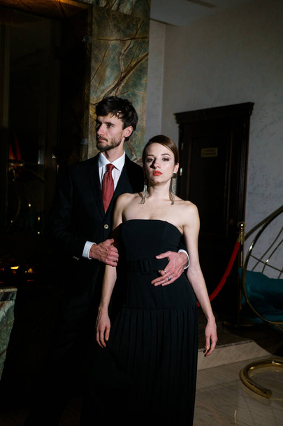 Tyylikäs mies ja nainen iltapuvussa, puku ja mekko, poseeraamassa ylellisen hotellin taustalla. Kasino käsite - Valokuva, kuva