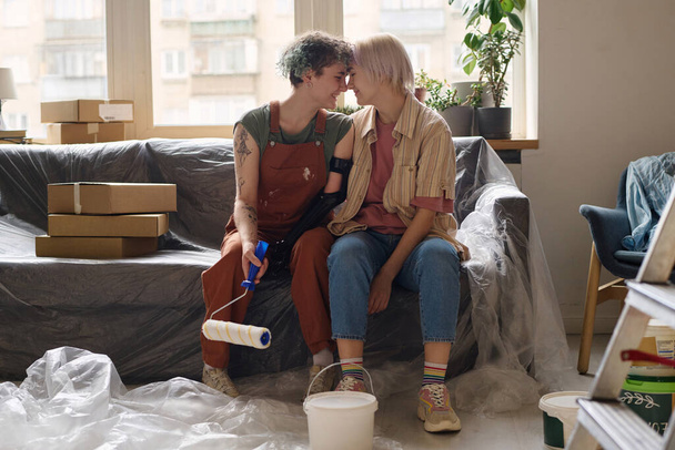 Lesbičky pár dělat opravy spolu v jejich novém bytě, sedí na pohovce a těší se navzájem - Fotografie, Obrázek