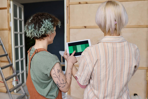 Vista trasera de las niñas apuntando al panel táctil y la elección de color verde para las paredes futuras en la nueva casa - Foto, imagen