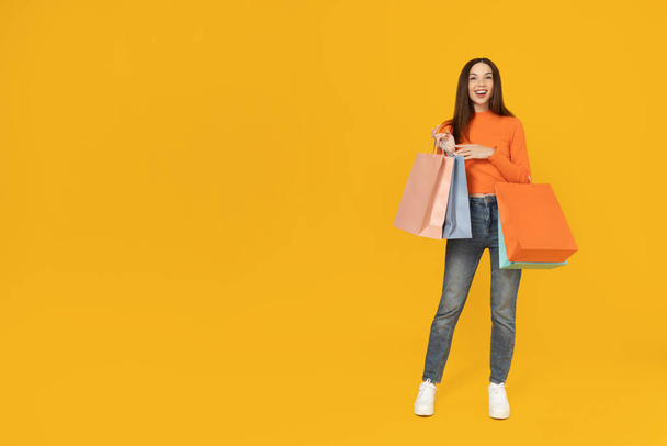Young girl with shopping bags on a yellow background. - Photo, Image