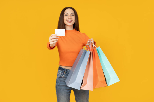 Young woman with paper bags and card on yellow background - Photo, Image