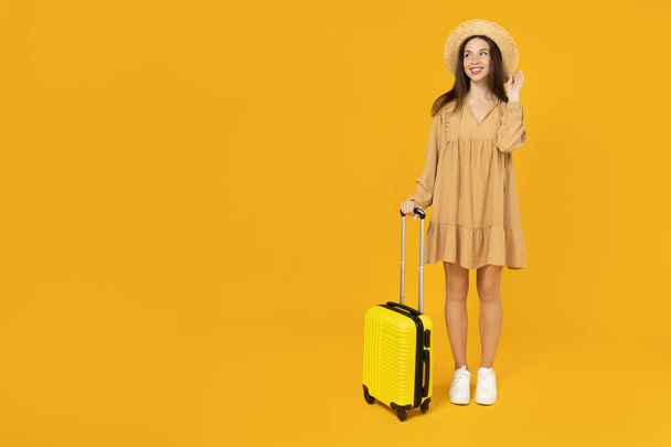 黄色の背景にスーツケースを持った少女. - 写真・画像