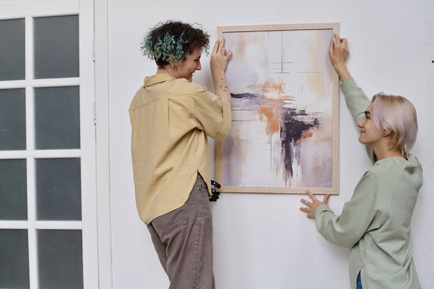 Νεαρές γυναίκες κρέμονται σύγχρονη ζωγραφική στον τοίχο στο δωμάτιο - Φωτογραφία, εικόνα