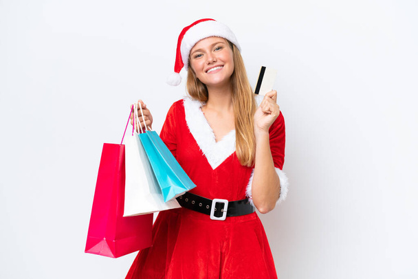 Young caucasian woman dressed as mama noel isolated on white background holding shopping bags and a credit card - Photo, Image