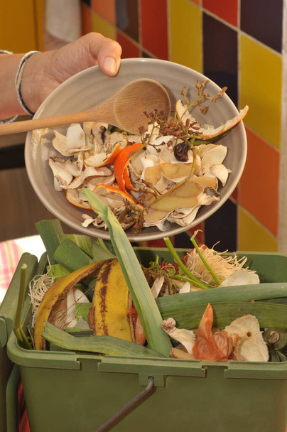 Jemand entleert einen Teller Biomüll in einen kleinen Kompostbehälter in der Küche - Foto, Bild