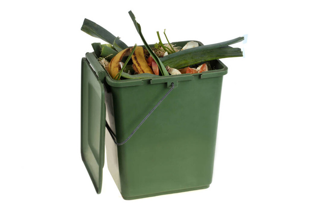 Concepto de compostaje con un recipiente de plástico verde lleno de residuos orgánicos de cerca sobre un fondo blanco - Foto, imagen