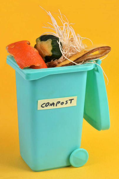 Concepto de compostaje con un bote de basura lleno de residuos orgánicos de cerca sobre fondo amarillo - Foto, imagen