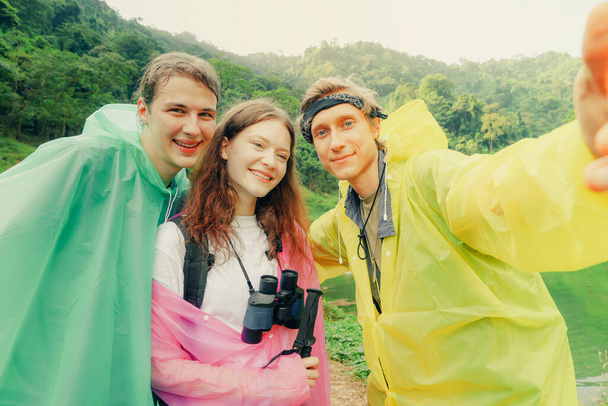 Portrait Amis proches, bel homme et belle femme caucasienne voyagent en randonnée pendant la saison des pluies et portent des imperméables ensemble en prenant des selfies hilarants en regardant joyeusement la caméra. - Photo, image