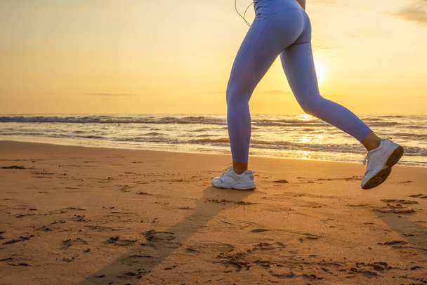 πόδια ενός κοριτσιού με μπλε κολάν και αθλητικά παπούτσια που τρέχουν κατά μήκος της παραλίας την αυγή με χώρο για επιγραφή. Υψηλής ποιότητας φωτογραφία - Φωτογραφία, εικόνα