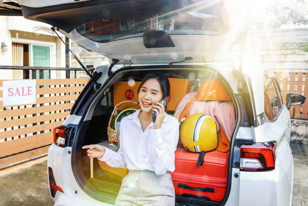 Retrato feliz hermosa mujer asiática que tuvo éxito en el trabajo moviendo el equipaje en el coche de atrás sentado y hablando por teléfono con su familia preparándose para salir a vivir en la nueva casa comprada. - Foto, imagen