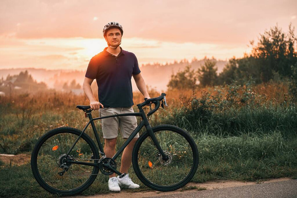 Μια σιλουέτα ενός ποδηλάτη κατάρτισης σε ένα μονοπάτι με ένα ποδήλατο χαλίκι, απολαμβάνοντας την περιπέτεια και την έννοια του αθλητισμού στο ηλιοβασίλεμα. - Φωτογραφία, εικόνα