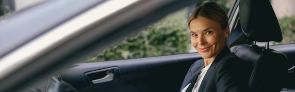 Gerente femenina sonriente se abrocha el cinturón de seguridad del coche mientras está sentado en el asiento del pasajero y se ve la cámara - Foto, Imagen