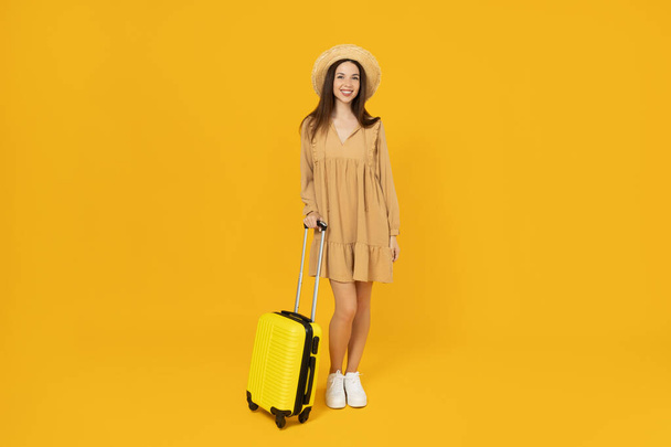 Νεαρό κορίτσι με μια βαλίτσα σε κίτρινο φόντο. - Φωτογραφία, εικόνα