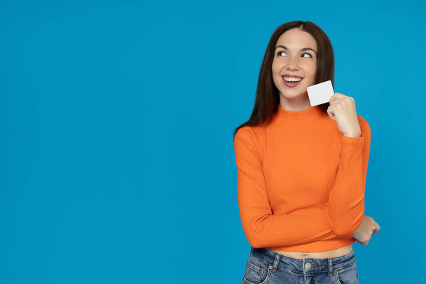 Chica joven feliz con una tarjeta en la mano sobre un fondo azul. - Foto, imagen