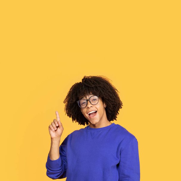 Eureka Concept. Portrait of emotional black student guy having great idea, finding inspiration, excited african american man in eyeglasses pointing finger up, standing on yellow studio background - Photo, Image