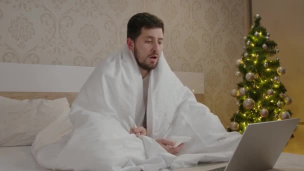 Mature man with beard got sick and works remotely on the computer at home. Entrepreneur works remotely. Boy wrapped in a white duvet coughs and sneezes loudly into a tissue and wipes his red nose - Footage, Video