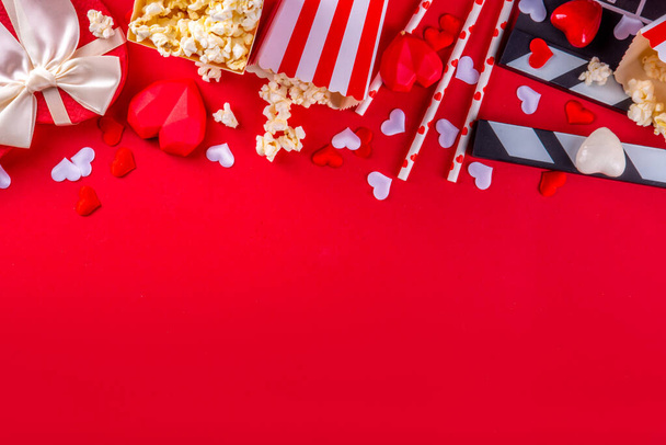 Romanttinen päivämäärä Ystävänpäivä 14 helmikuu. Rakkausmaraton, treffit elokuvateatterissa. Clapperboard, popcorn kauhat, sydän sisustus ja suklaata punaisella taustalla tasainen lay kopio tilaa - Valokuva, kuva