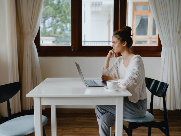 Creatieve jonge vrouw werkt aan een bureau thuis in een gezellig interieur met een kopje drank, thuiskantoor freelancer met een glimlach, communicatie en onderwijs online. Hoge kwaliteit foto - Foto, afbeelding