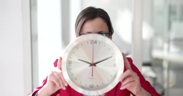 Une femme d'affaires dans le bureau tient une grande horloge murale, un gros plan. Concept heures supplémentaires, délai - Séquence, vidéo