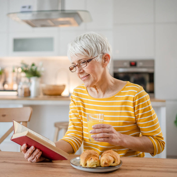 Yksi nainen kypsä vanhempi valkoihoinen naispuolinen eläkeläinen moderni isoäiti luki kirjaa kotona kulumista silmälasit todellinen henkilö kopioi tilaa - Valokuva, kuva