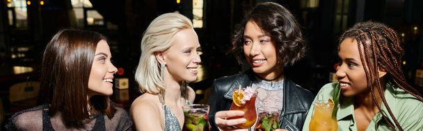 smiling multiethnic women holding cocktail glasses while spending time in bar, horizontal banner - Photo, Image