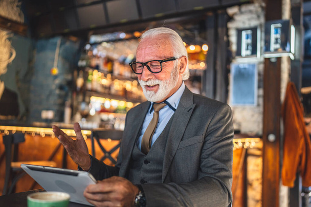 Один старший чоловік кавказький чоловік бізнесмен власник використовує цифровий планшет сидить в кафе відеозв'язок і комунікаційний одяг костюм костюм копіювати простір
 - Фото, зображення
