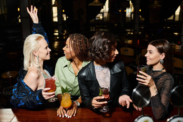 усміхнені багаторасові модниці з коктейлями розмовляють під час вечірки в барі, дружби та дозвілля - Фото, зображення