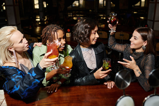 весела жінка тости з коктейлем біля багаторасових подружок в барі, яскравий спосіб життя - Фото, зображення