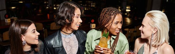 happy and trendy multiracial girlfriends with cocktail glasses talking in bar, horizontal banner - Photo, Image