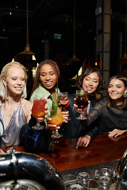 вечірка курки в барі, молоді багаторасові модниці посміхаються і тости в келихах коктейлів - Фото, зображення