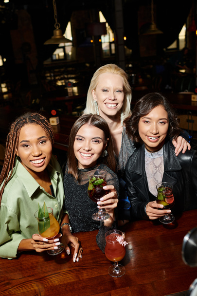 Moda ve mutlu çok ırklı bayan arkadaşlar ellerinde lezzetli kokteyller ve barda kameraya bakıyorlar. - Fotoğraf, Görsel