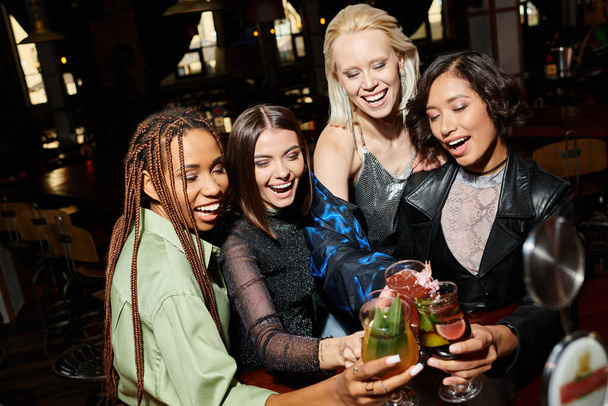 podekscytowane i młode wielokulturowe kobiety brzęczące pyszne koktajle w barze, happy party time - Zdjęcie, obraz