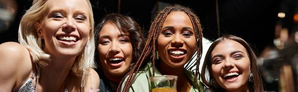 groupe diversifié de copines multiethniques souriant à la caméra dans le bar de nuit, bannière horizontale - Photo, image