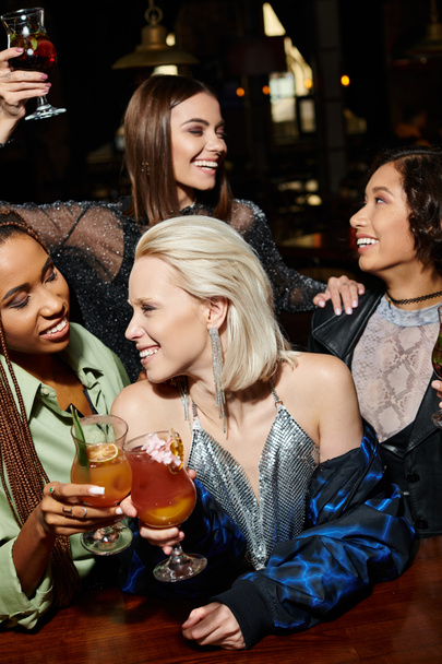 Barda parti sırasında etnik çeşitliliğe sahip kız arkadaşlarının yanında kokteyl bardaklarını tokuşturan kadınları mutlu etmek. - Fotoğraf, Görsel