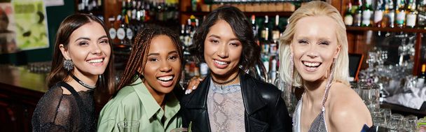 радісні і стильні багатоетнічні подружки з коктейльними окулярами, які дивляться на камеру в барі, банер - Фото, зображення