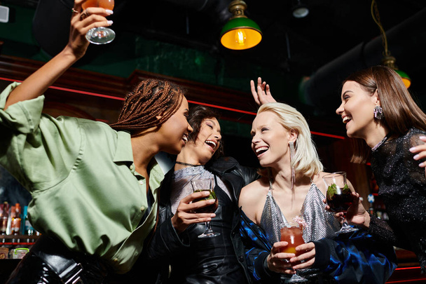fröhliche und stilvolle multikulturelle Freundinnen mit Cocktailgläsern tanzen in der Bar, Party Time - Foto, Bild