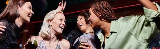 joyful and fashionable multicultural girlfriends with delicious cocktails dancing in bar, banner - Photo, Image